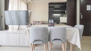 Ein Hotelzimmer mit Flachbildfernseher, Minibar, Tisch mit weißer Tischdecke und zwei grau gepolsterten Sesseln.