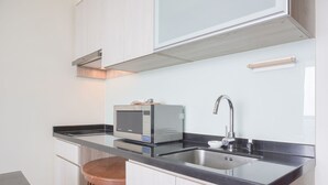A modern kitchen with a microwave, sink, and wooden stool. - Nice And Elegant 2Br At 26Th Floor Menteng Park Apartment (Jakarta)