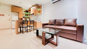 A modern living room with a glass coffee table, leather sofa, and wooden dining set. - Elegant And Spacious 2Br At Paddington Heights Apartment (Tangerang)