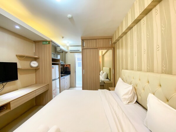 A hotel room with a bed, a TV, a desk, a wardrobe, and a bathroom visible through an open door.
