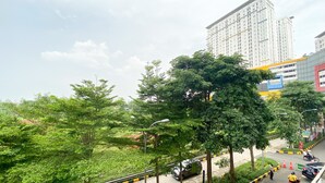 A street with trees, a road, and a tall building in the background. - Cozy And Comfy Studio At Bassura City Apartment (Jakarta)