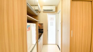 A narrow hallway with wooden cabinets, a white door, and an air conditioning unit on the ceiling. - Cozy And Comfy Studio At Bassura City Apartment (Jakarta)