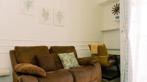 A brown leather sofa with cushions, a small table with a chair, and wall art.