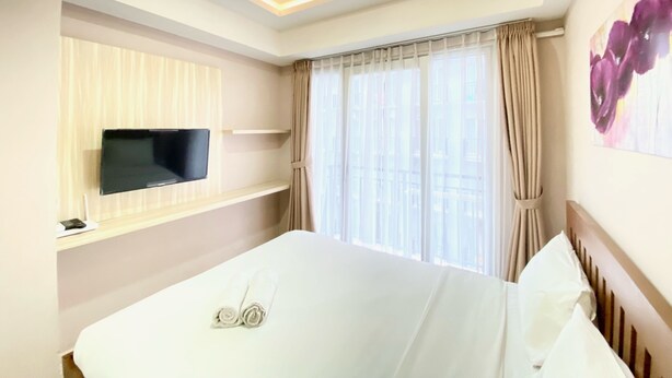 Ein Hotelzimmer mit Bett, Flachbildfernseher an der Wand, Fenster mit Vorhängen und Deckenleuchte.