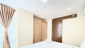 A hotel room with a large bed, a wooden wardrobe, and a door with a mirror. - Spacious 2Br Apartment At Grand Asia Afrika (Bandung)