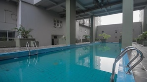An indoor swimming pool with clear blue water, surrounded by tiled walls and pillars. - Spacious 2Br Apartment At Grand Asia Afrika (Bandung)