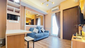 A modern living room with a blue sofa, wooden flooring, a small table, and a built-in TV. - Best Choice And Comfy 2Br At Transpark Bintaro Apartment (South Tangerang)