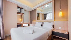 A neatly made bed with a white comforter and a rolled white towel, a bedside table with a lamp, and a large mirror above the bed. - Best Choice And Comfy 2Br At Transpark Bintaro Apartment (South Tangerang)