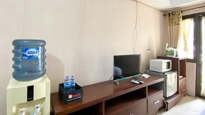 Habitación de hotel con un dispensador de agua grande, televisión de pantalla plana, microondas y refrigerador pequeño.