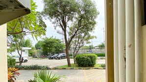 Vista desde un balcón sobre un estacionamiento con varios coches, un edificio blanco y árboles verdes.