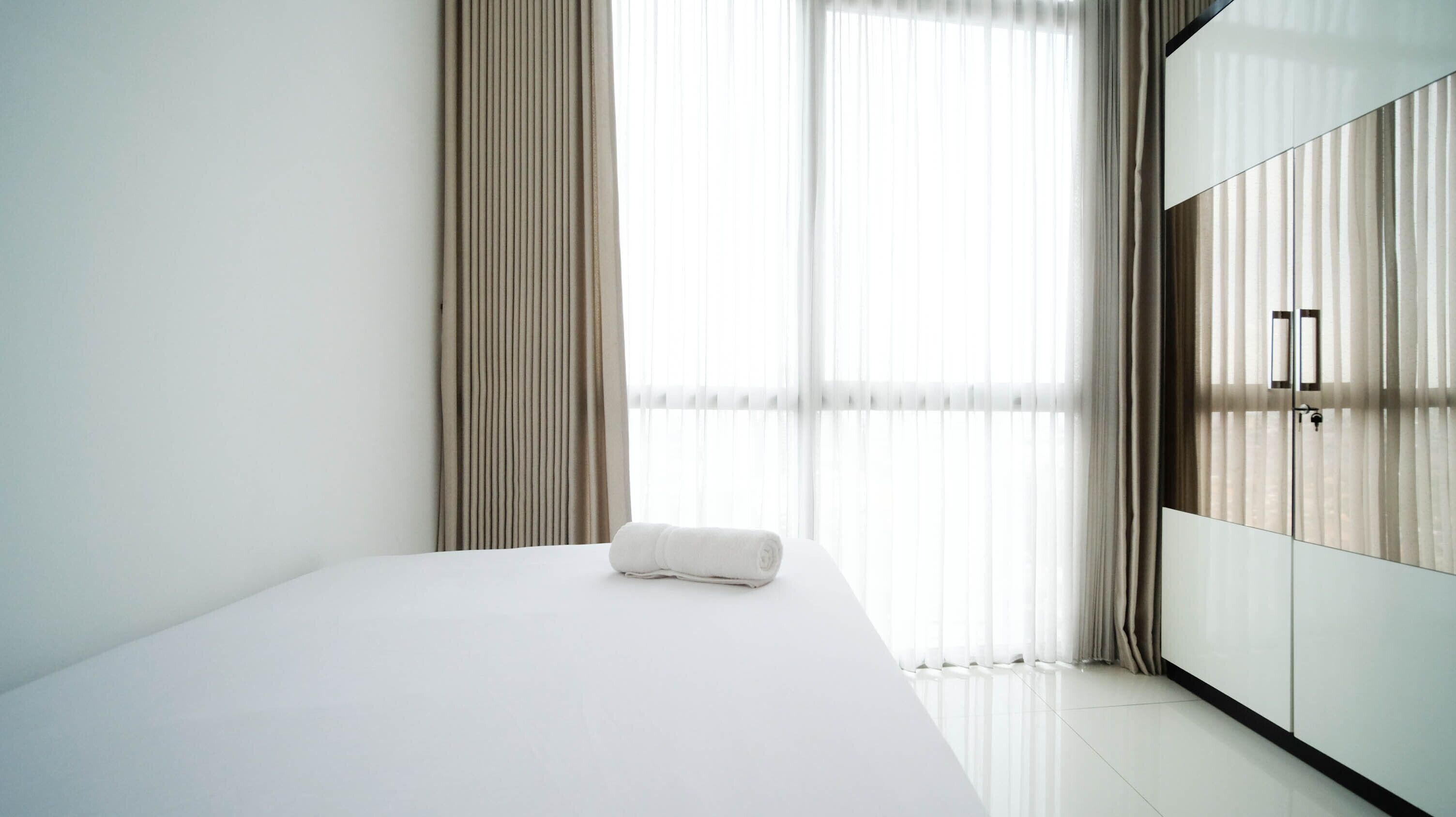 A hotel room with a bed, a wardrobe, and sheer curtains.
