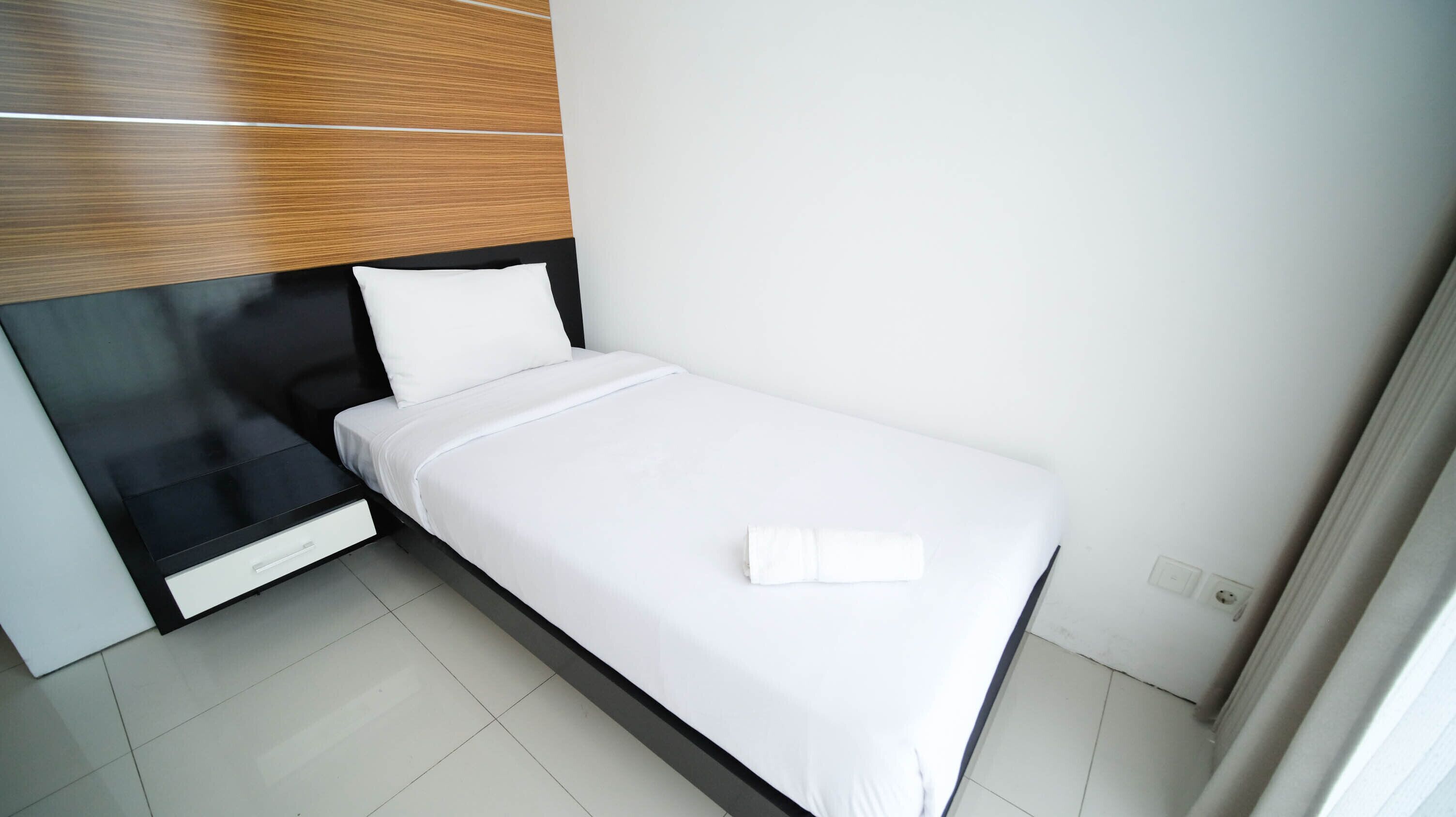 A small, modern bedroom with a bed, a nightstand, and a wooden headboard.