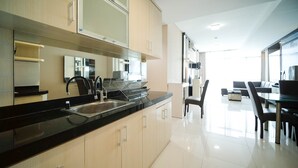 A modern kitchen with a black countertop, stainless steel sink, and light wood cabinets. There is a dining area with a glass table and chairs.