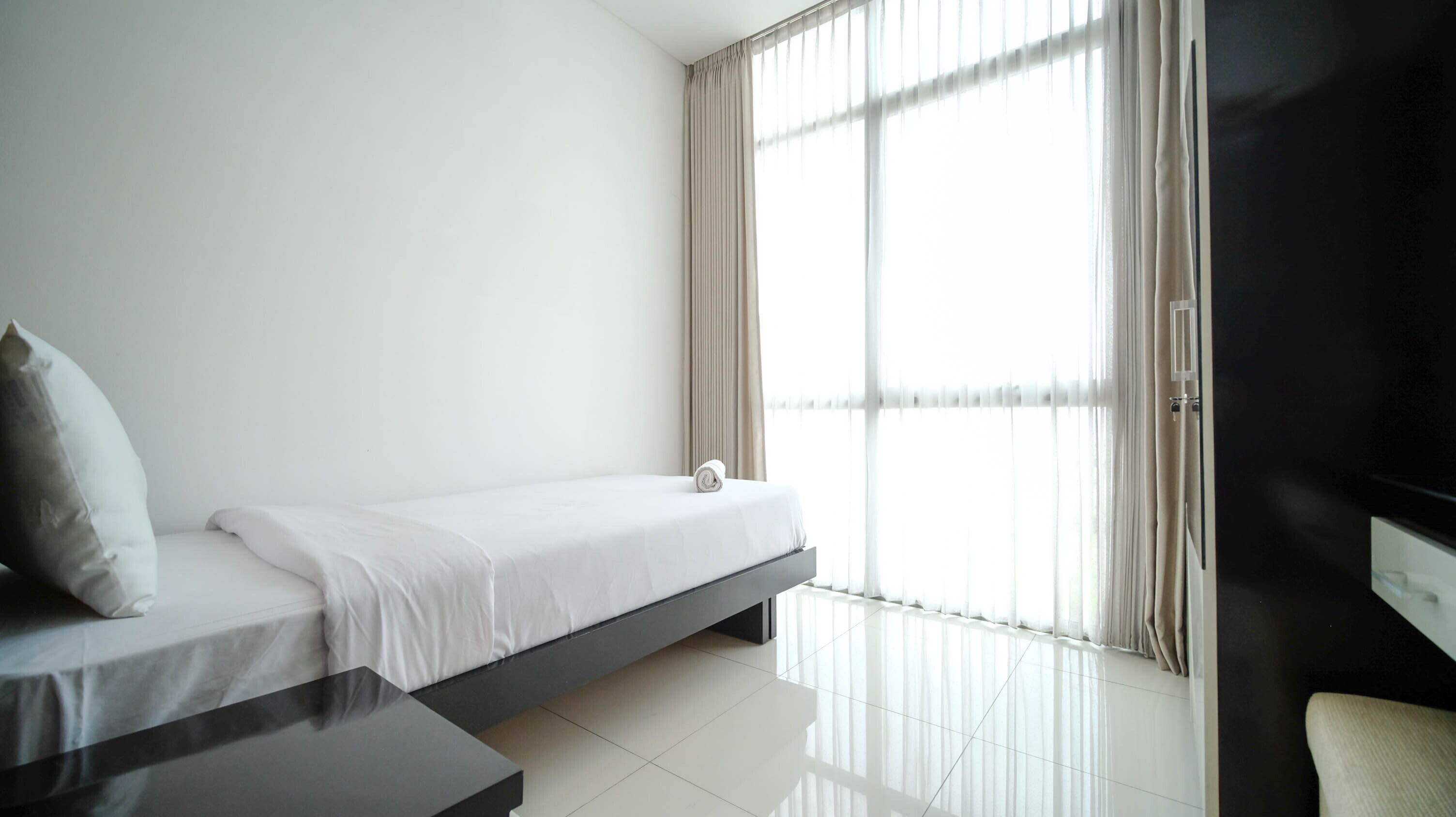 Habitación de hotel minimalista con cama, una mesita pequeña y un ventanal con cortinas.