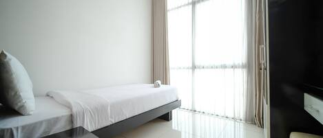 Habitación de hotel minimalista con cama, una mesita pequeña y un ventanal con cortinas.