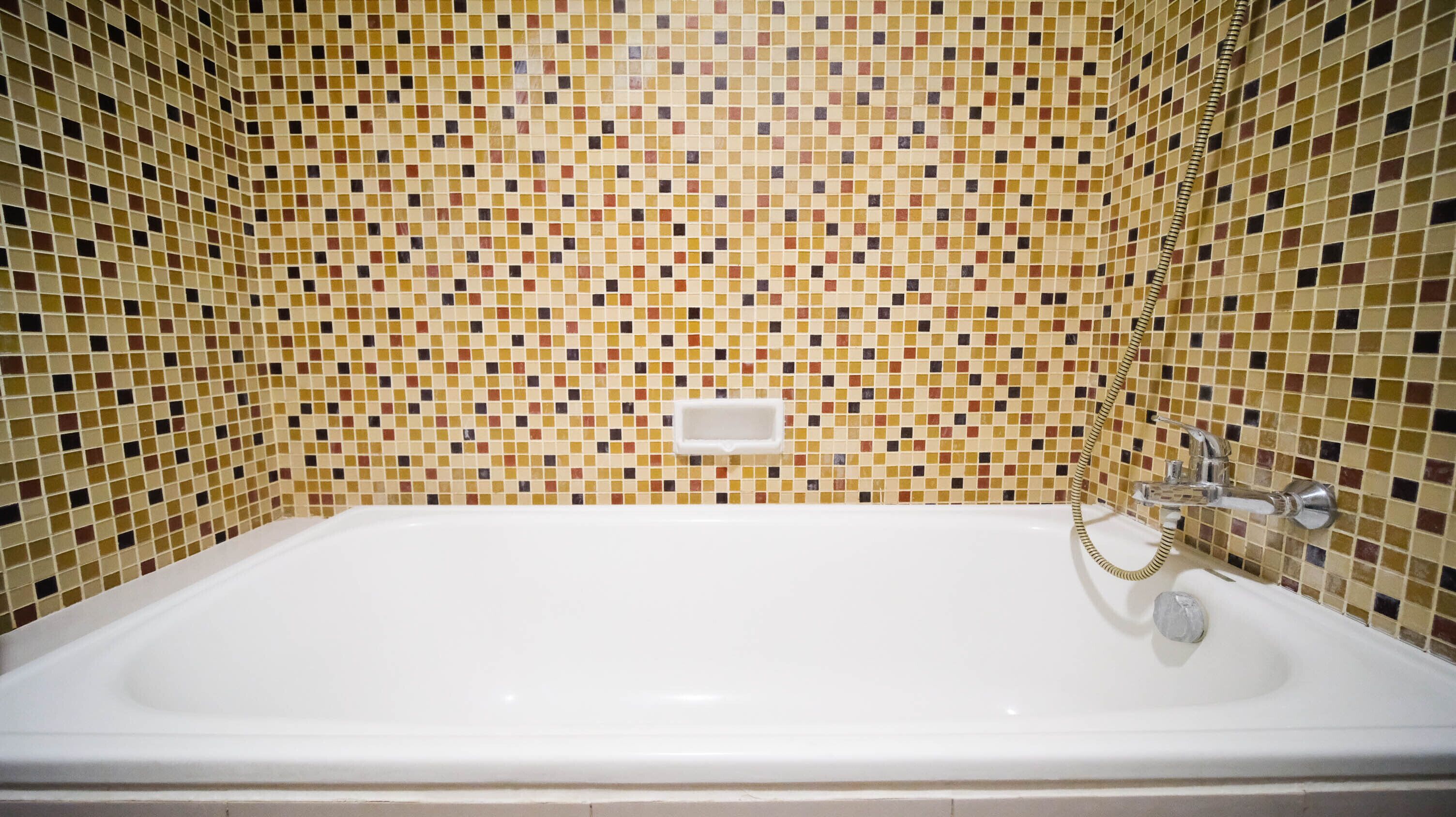 Un bagno con una vasca da bagno bianca, una doccia dotata di rubinetteria cromata e una parete rivestita di mosaico.