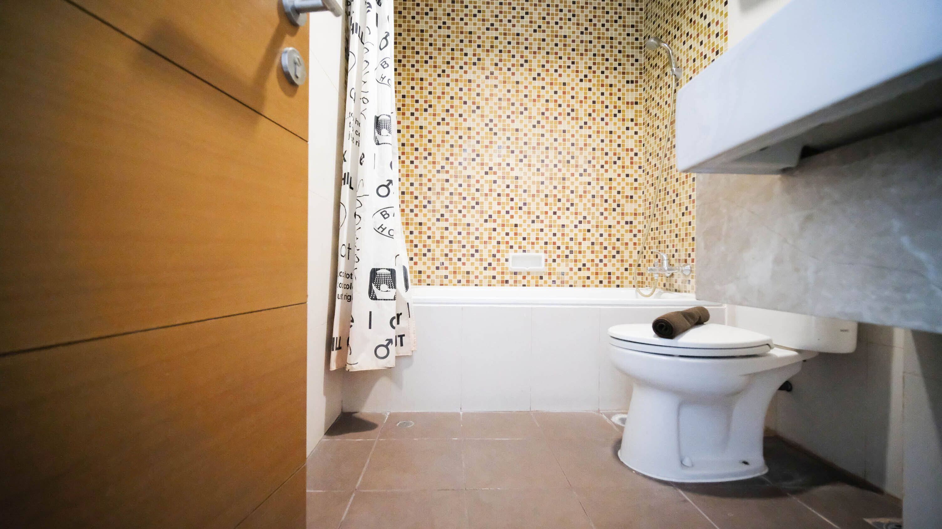 Une salle de bain avec des toilettes blanches, un espace douche et un mur carrelé.