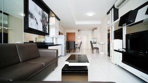 A modern living room with a sofa, a coffee table, a TV, and a kitchen area in the background.