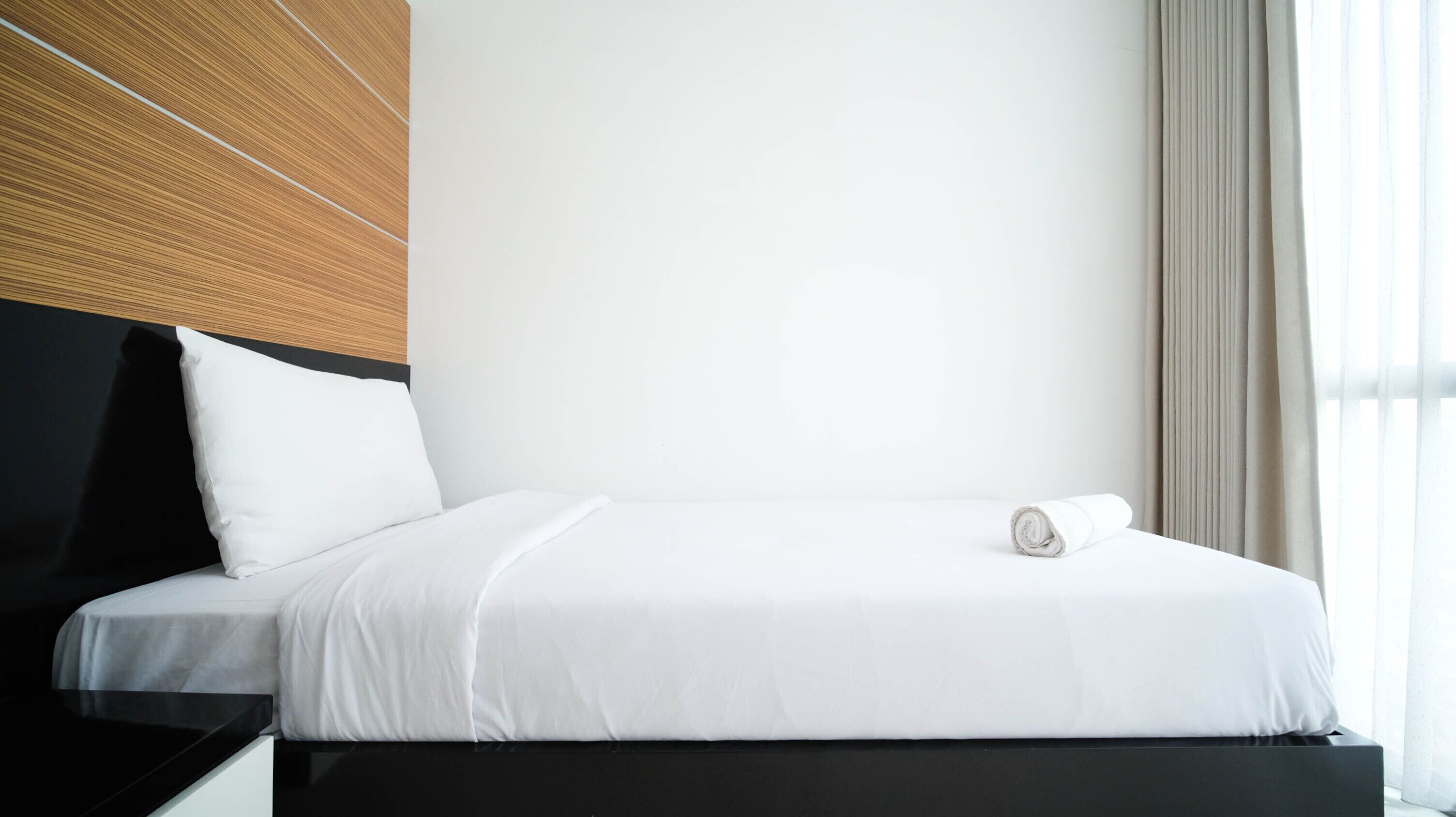 Ein modernes Hotelzimmer mit einem ordentlich bezogenen Bett, einem schwarzen Kopfteil und einem großen Fenster mit Vorhängen.