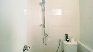 A bathroom with white tiled walls, a shower with a handheld showerhead, a toilet with a bidet attachment, and a door with a metallic handle.