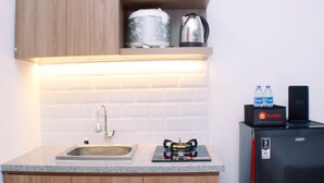A kitchen with a granite countertop, a sink, wooden cabinets, a stove, a kettle, a water dispenser, and a refrigerator.