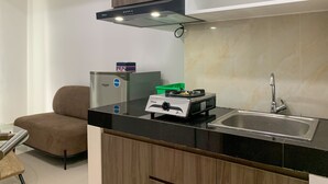 A compact kitchen with a black countertop, stainless steel sink, and a compact refrigerator. - Homey And Simply 2Br At Serpong Garden Apartment (Cisauk)
