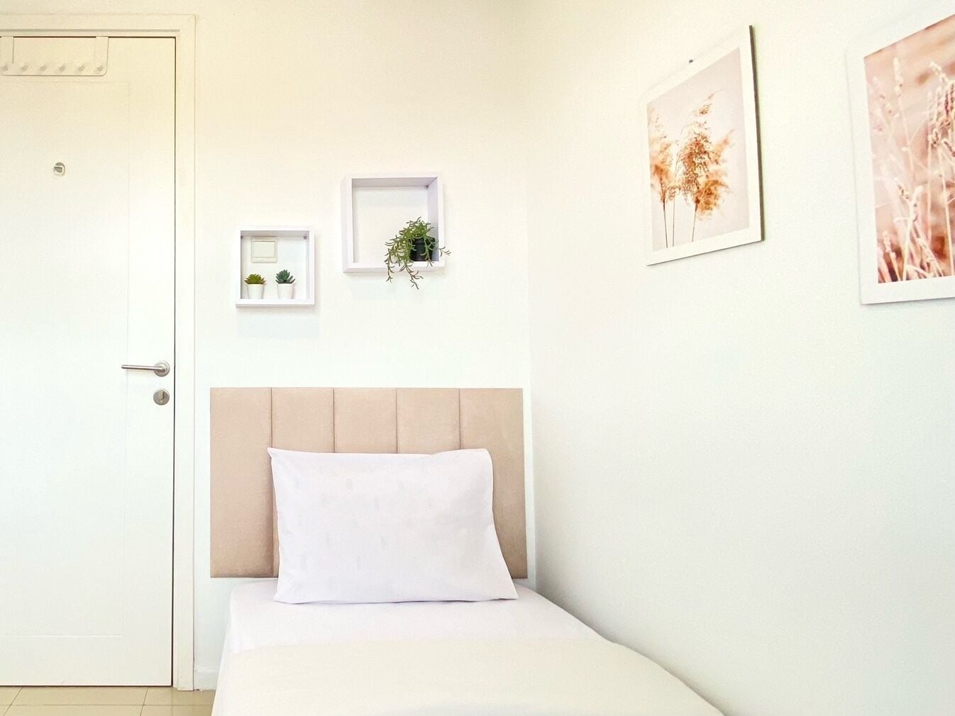 Een minimalistische slaapkamer met een enkel bed, een witte deur en een klein plankje met planten.