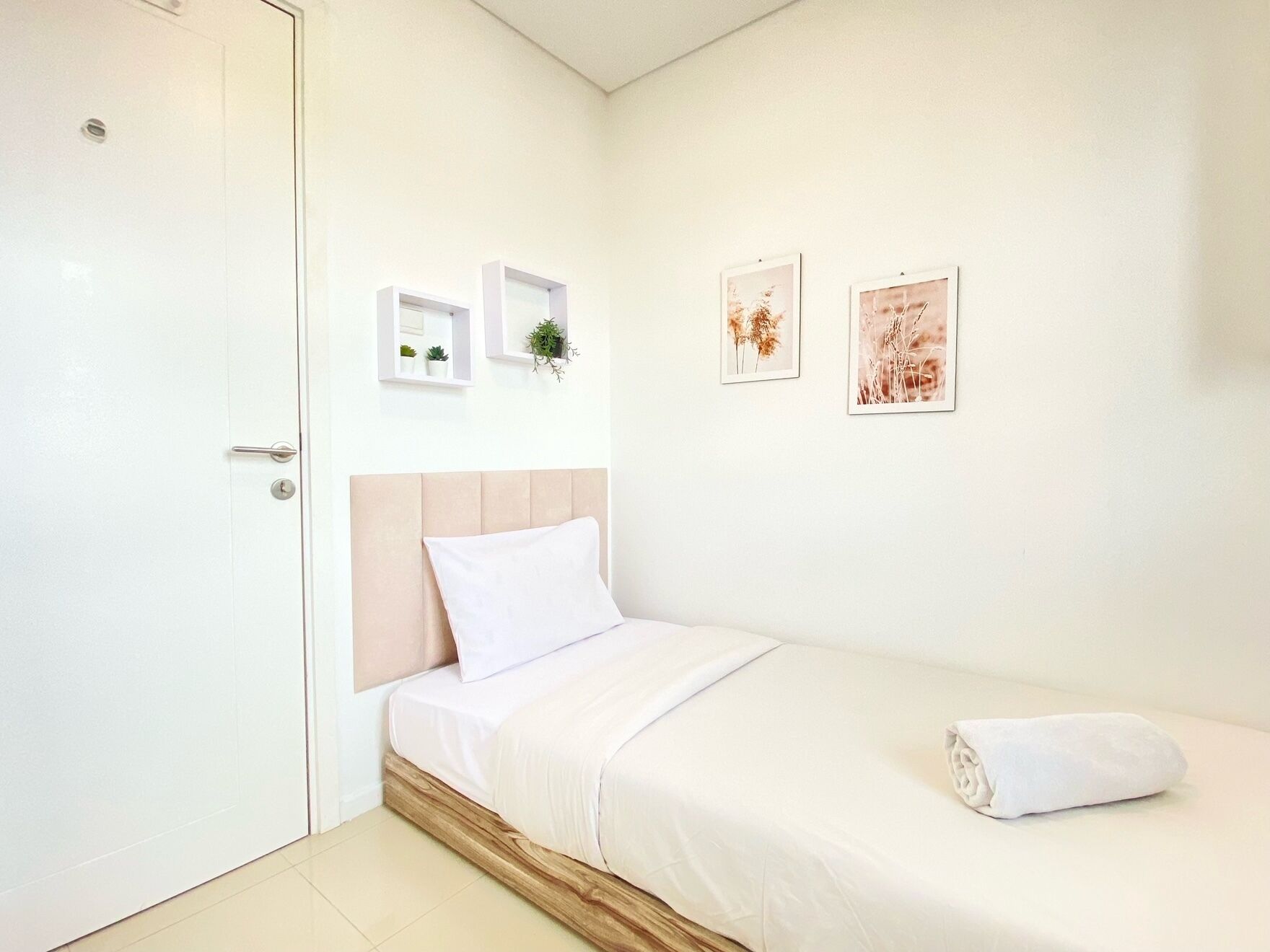 Un dormitorio con cama, una puerta y dos estantes en la pared con plantas e imágenes.