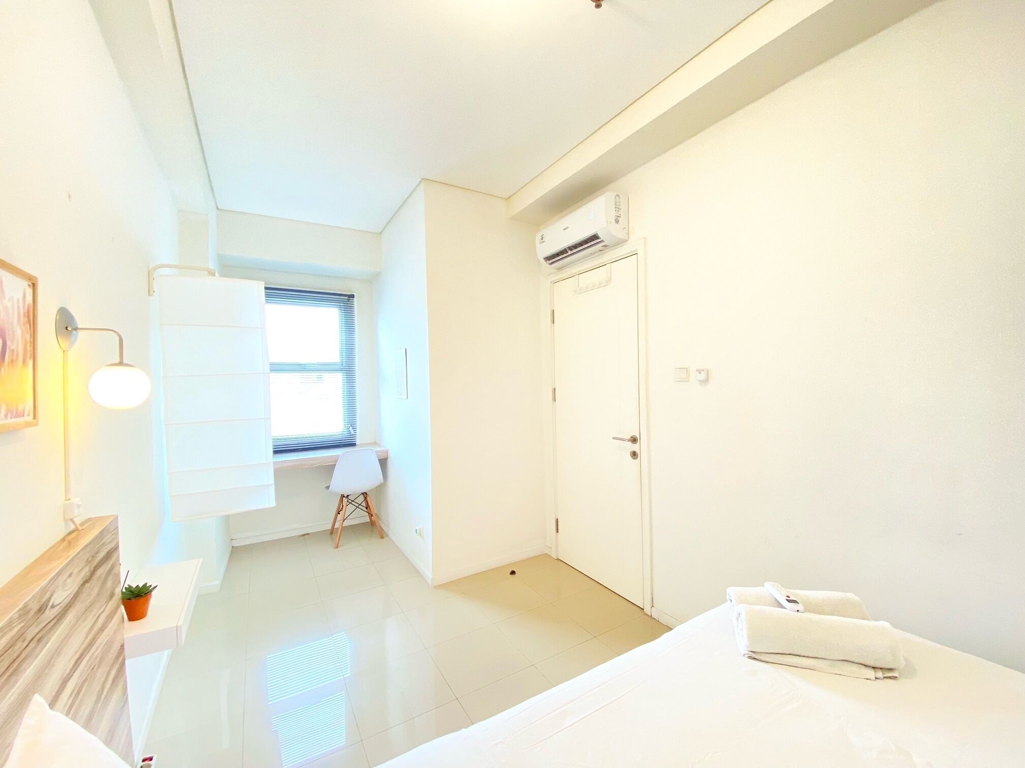 Ein heller, minimalistischer Hotelraum mit Bett, Schreibtisch und einem Fenster mit Jalousien.