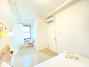 Ein heller, minimalistischer Hotelraum mit Bett, Schreibtisch und einem Fenster mit Jalousien.
