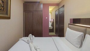 Une chambre d’hôtel avec un lit bien fait, une armoire, un miroir et une porte donnant sur une autre pièce.