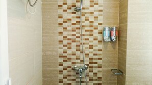 A shower with a tiled wall, a handheld showerhead, and a wall-mounted faucet. There are toiletries on the wall.