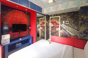 Habitación de hotel con una cama grande, un televisor montado en una pared roja y decoración temática de Spider-Man.