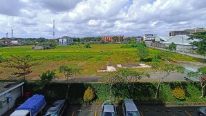 A parking lot with several cars, a green field, and buildings in the background.