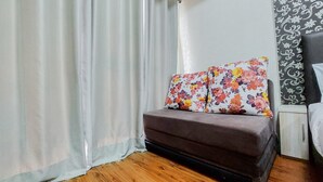 Una stanza con un divano letto, cuscini floreali, pavimento in legno e parete decorata.
