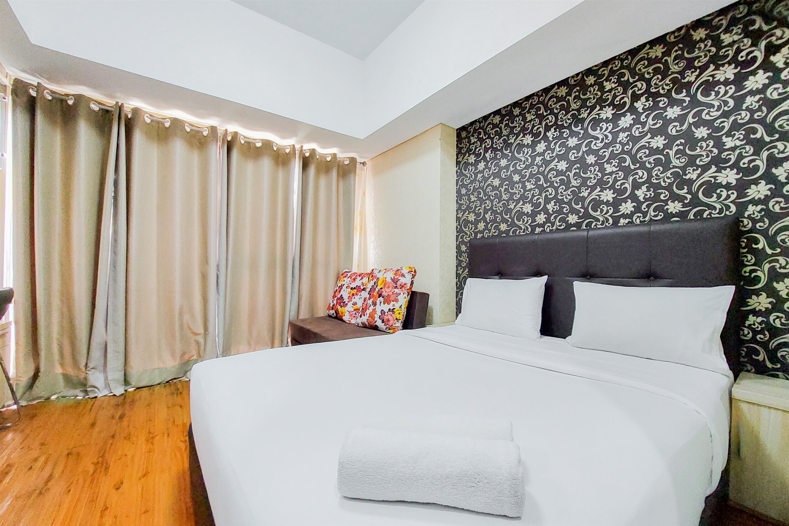 Een hotelkamer met een groot bed, nachtkastje, stoel en behang met een patroon.