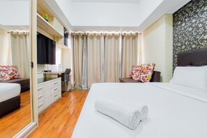 Quarto de hotel com cama grande, escrivaninha, cadeira e televisão.