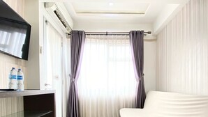 Una habitación de hotel moderna con un televisor de pantalla plana, un sofá y una ventana con cortinas translúcidas.