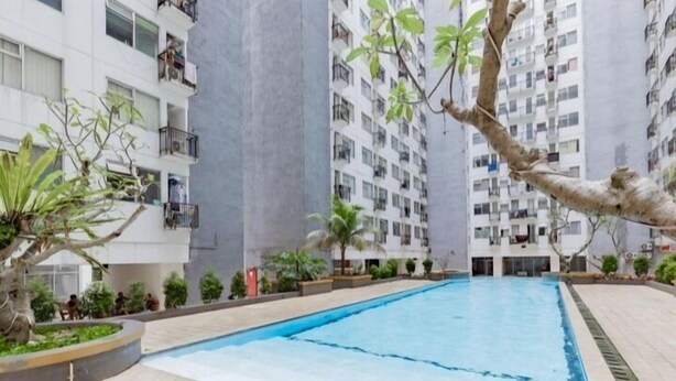 Una piscina rodeada de edificios residenciales con balcones, árboles y un jardín bien cuidado.