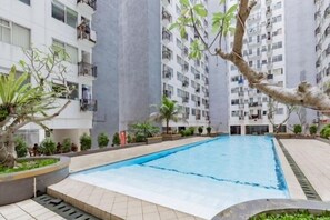 A swimming pool surrounded by residential buildings with balconies, trees, and a well-maintained garden area. - Modest 2Br Apartment At Jarrdin Cihampelas (Bandung)