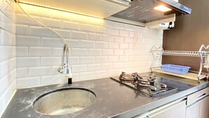Una cocina con azulejos blancos tipo metro, un lavamanos de acero inoxidable, una estufa a gas y una campana extractora.