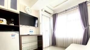 Habitación de hotel con televisión de pantalla plana, refrigerador, reloj, ventana con cortinas y cama.
