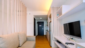 A modern living room with a sofa, a TV, and a wooden floor. - Nice Living Studio At 8Th Floor Tamansari The Hive Apartment (Jakarta)