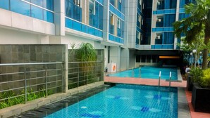 A swimming pool with tiled flooring, surrounded by a stone wall and metal railings. - Nice Living Studio At 8Th Floor Tamansari The Hive Apartment (Jakarta)