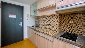 A kitchen with wooden cabinets, a tiled backsplash, a stainless steel sink, and a gas stove. - Nice Living Studio At 8Th Floor Tamansari The Hive Apartment (Jakarta)