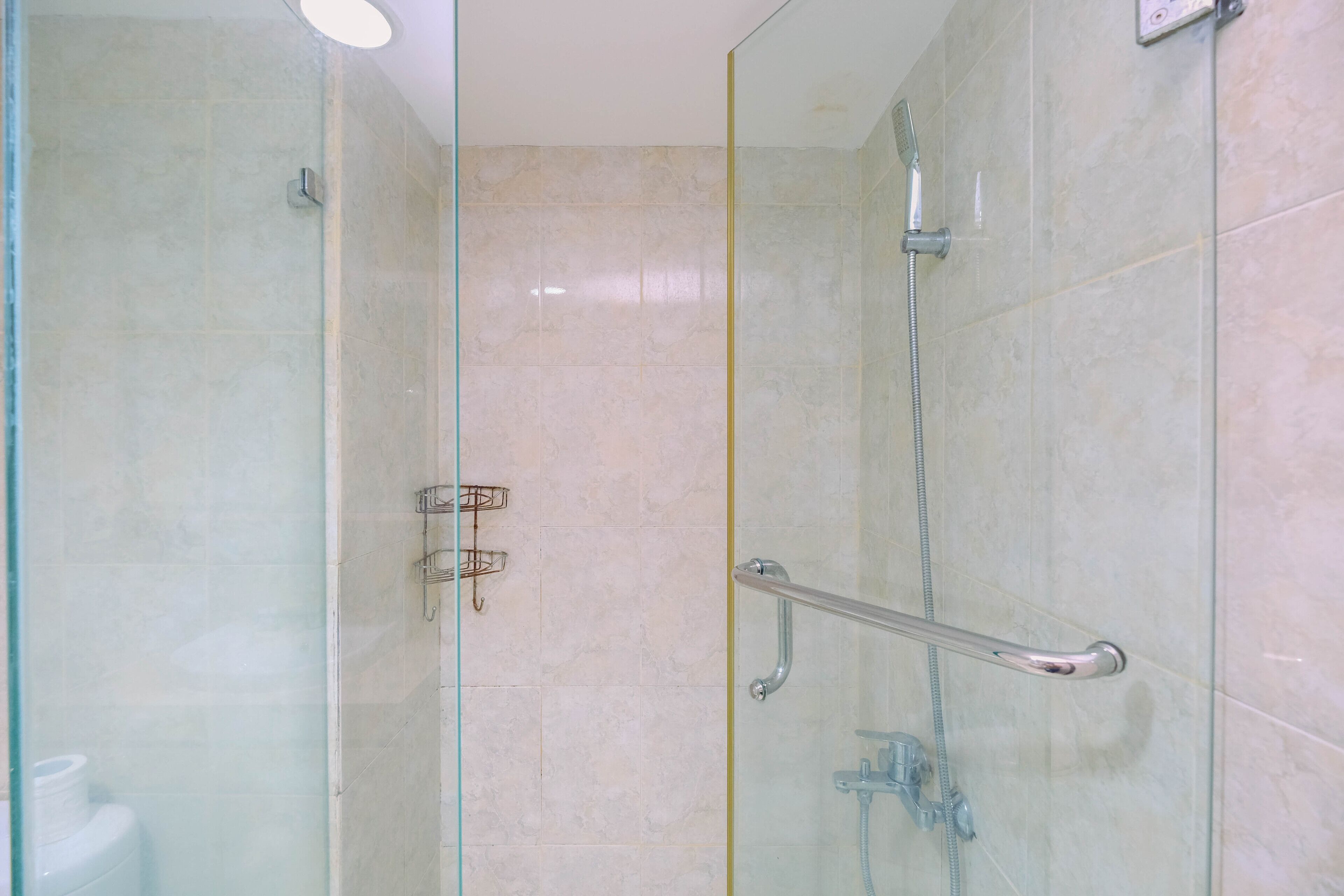 A glass-enclosed shower area with a handrail, a handheld showerhead, and a wall-mounted faucet.