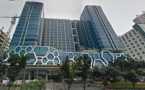A modern hotel with a distinctive geometric facade, multiple high-rise buildings in the background, and a well-maintained outdoor area with trees. - Nice Living Studio At 8Th Floor Tamansari The Hive Apartment (Jakarta)
