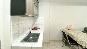 A small kitchen with a sink, a red kettle, and a table with a lace tablecloth. - Elegant And Comfy 2Br Springlake Summarecon Bekasi Apartment Near Summarecon Mall (Bekasi)