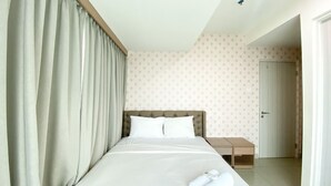 A hotel room with a large bed, a wooden nightstand, a door, and a patterned wall. - Fancy And Nice 3Br At Grand Kamala Lagoon Apartment (Bekasi)