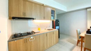 A modern kitchen with wooden cabinets, a gas stove, a built-in oven, a refrigerator, and a dining area with a table and chairs. - Fancy And Nice 3Br At Grand Kamala Lagoon Apartment (Bekasi)